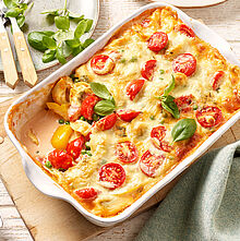 Vegetarischer One-Pot-Tortelliniauflauf frisch aus dem Backofen in einer weißen Auflaufform, garniert mit frischem Basilikum