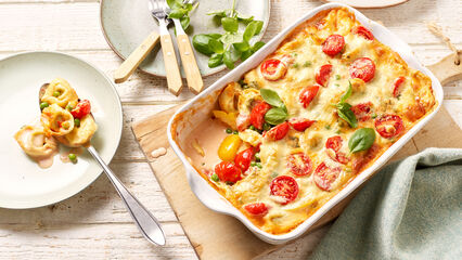 Vegetarischer One-Pot-Tortelliniauflauf frisch aus dem Backofen in einer weißen Auflaufform, garniert mit frischem Basilikum