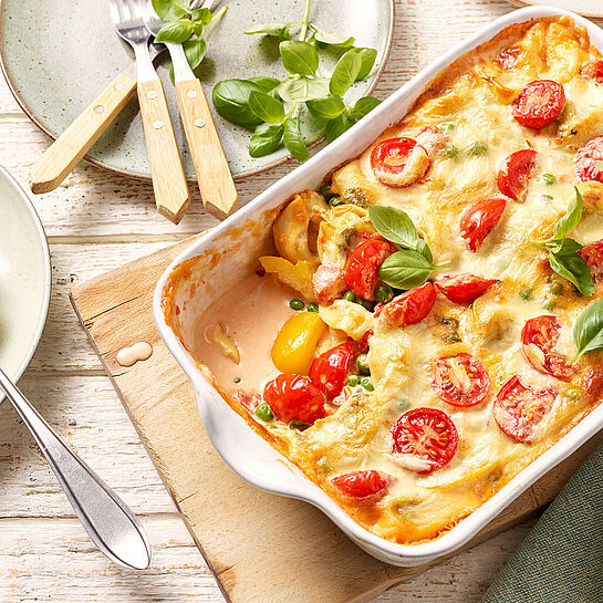 Vegetarischer One-Pot-Tortelliniauflauf frisch aus dem Backofen in einer weißen Auflaufform, garniert mit frischem Basilikum