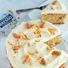 Saftiger Karottenkuchen mit cremigem BRESSO-Frosting, dekoriert mit Walnüssen und Marzipankarotten, auf einem weißen Teller.