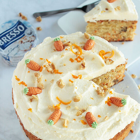 Saftiger Karottenkuchen mit cremigem BRESSO-Frosting, dekoriert mit Walnüssen und Marzipankarotten, auf einem weißen Teller.