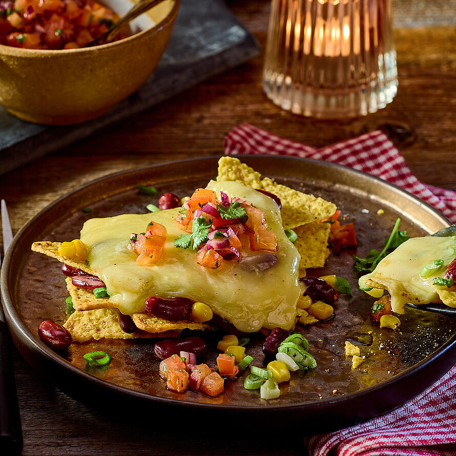 Leckeres Raclettegericht mit knusprigen Tortilla-Chips, geschmolzenem Raclette-Käse, Mais, Bohnen und einer frischen Tomatensalsa, verfeinert mit Koriander.