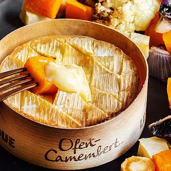 Gebackener Camembert umgeben von farbenfrohem, geröstetem Gemüse – ein kulinarisches Stillleben aus Cremigkeit und Frische.