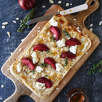 Knuspriger Flammkuchen belegt mit Ziegenfrischkäse, saftigen Pflaumen, Mandeln und einem Hauch Honig, perfekt für Genießer.