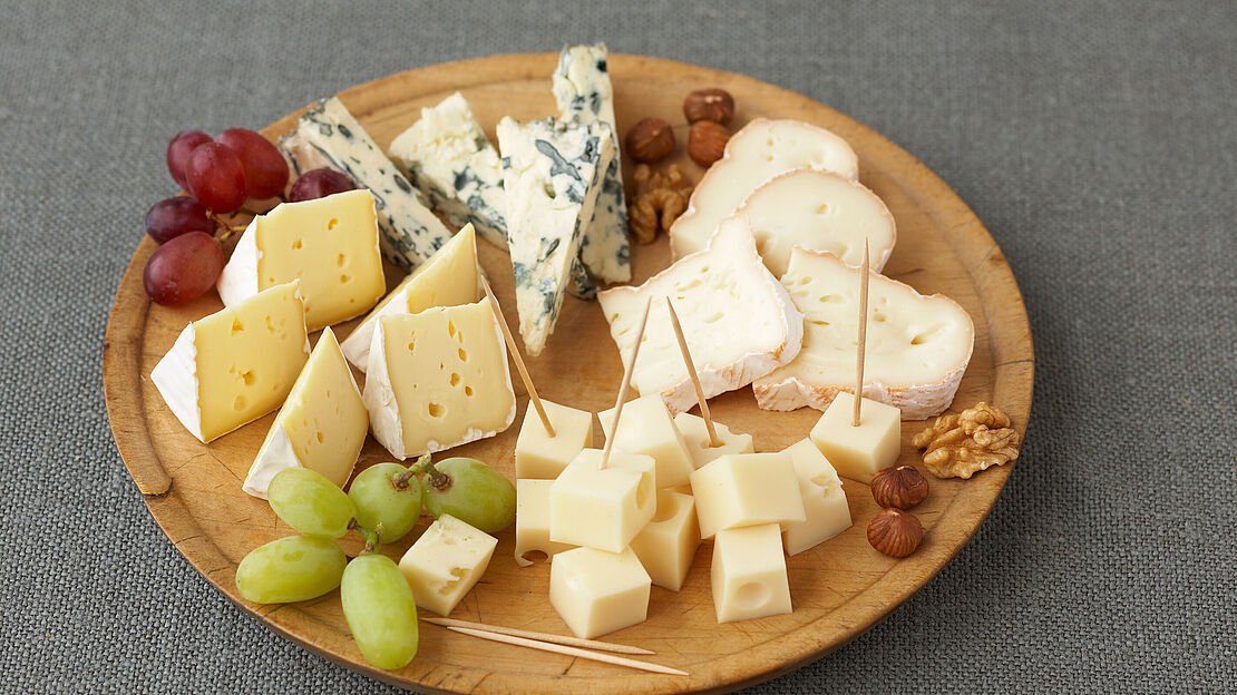 Kleine Holzservierplatte mit verschieden Käsesorten, Trauben und Nüssen.  