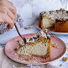 Ein Stück köstlicher Rhabarber-Streuselkuchen mit cremiger Frischkäsefüllung und knusprigen Streuseln auf einem rosa Teller.