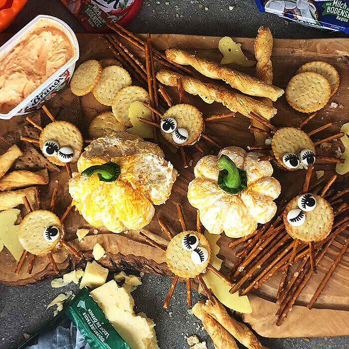 Käsekürbisse, lustige Spinnen-Cracker-Smileys und Gemüse zum Dippen auf einer Holzplatte. Ein pfiffiges Käse-Fingerfood-Rezept! 