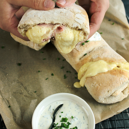 Frisch gebackenes Handbrot wie vom Weihnachtsmarkt, gefüllt mit schmelzendem Raclettekäse und Schinken, serviert mit cremigem Dip.