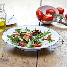 Frischer Rucola Salat mit gebratenen Auberginen, Datteltomaten und gehobeltem Parmesan. Dressing aus Aceto Balsamico, Olivenöl und Senf. 