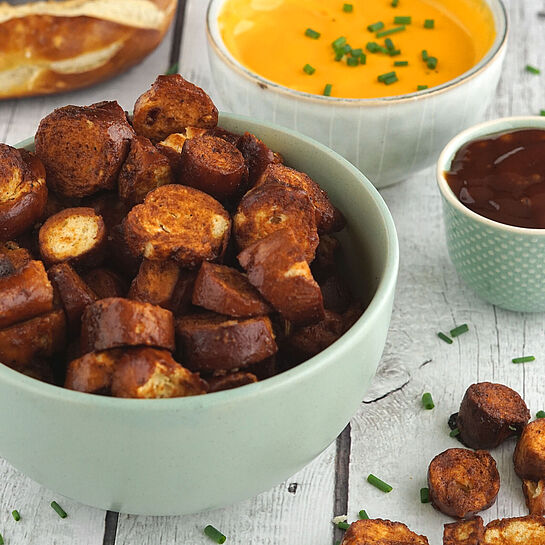 Knusprige Brezelstücke mit BBQ-Sauce im Schälchen, serviert mit cremiger Cheddar-Käsesauce. 