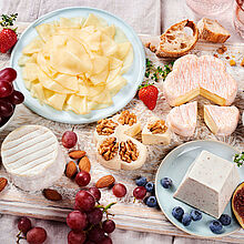 Fein angerichtete Käseplatte mit Sorten wie Saint Albray, Ziegenfrischkäse und Fol Epi, umgeben von frischen Früchten und Nüssen.