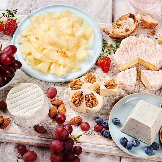 Fein angerichtete Käseplatte mit Sorten wie Saint Albray, Ziegenfrischkäse und Fol Epi, umgeben von frischen Früchten und Nüssen.