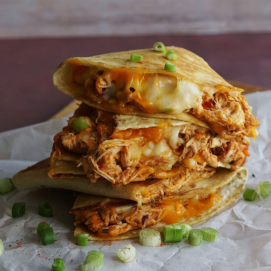 Knusprig gebratene Quesadillas mit geschmolzenem Cheddar und zartem Pulled Chicken, serviert auf einem Holzbrett.