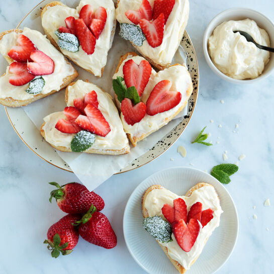 Herzförmige Plunderteilchen mit Frischkäsecreme und frischen Erdbeeren auf hellem Untergrund