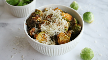 Gerösteter Rosenkohl mit frisch geriebenem Parmesan in einer weißen Schüssel.