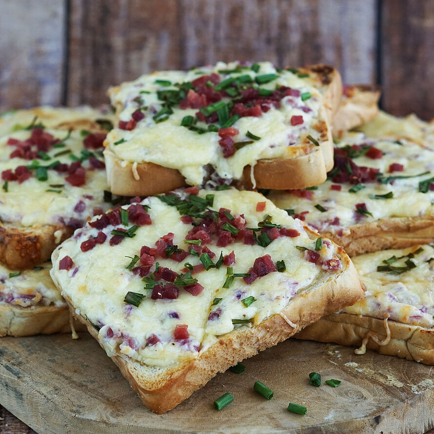 Knuspriger Flammkuchen-Toast mit Schinken, Gouda und Zwiebeln, frisch aus dem Ofen und garniert mit Schnittlauch.