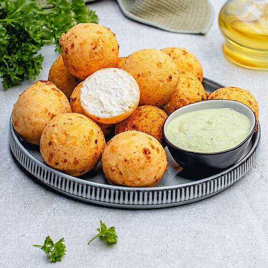 Goldbraune kolumbianische Buñuelos - Feta-Bällchen auf einem Teller, knusprig frittiert und bereit zum Genießen.