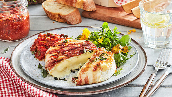 Camembert Gegrillt mit Kräuter-Speck & Tomatenchutney Le Rustique Camembert im Kräuter-Speckmantel, serviert mit Tomatenchutney und Wildkräutersalat. Dazu frisches Baguette und Wasser mit Zitrone.