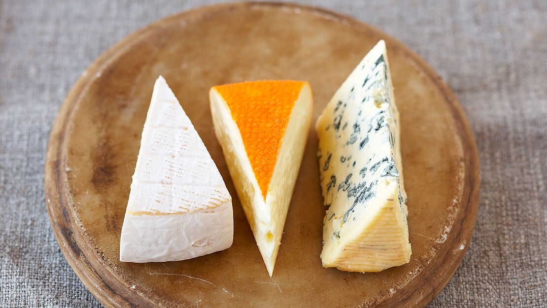 Käsewissen: Schimmelkäse sorgt für eine individuelles Aroma Runde rustikale Holzkäseplatte mit drei Variationen von Schimmelkäse am Stück