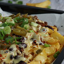 Chilli Cheese Fries serviert auf einem schwarzen Teller  –  Knusprige Pommes Frites, belegt mit würzigem Rinderhackfleisch, geschmolzenem Fol Epi Käse und scharfen Jalapeños.