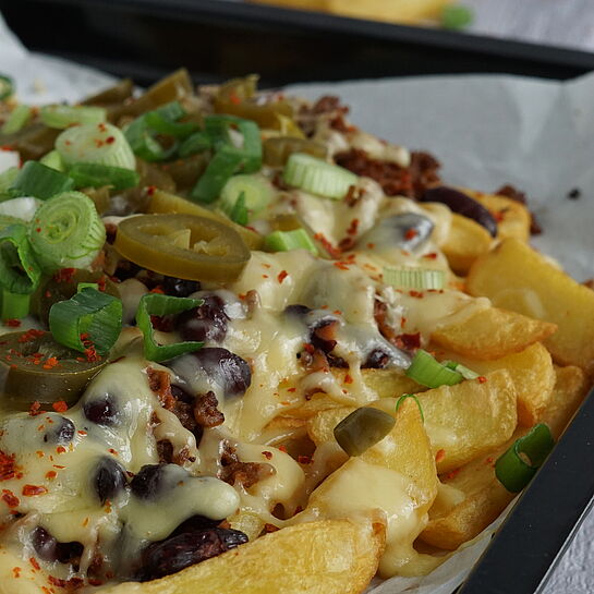 Chilli Cheese Fries serviert auf einem schwarzen Teller  –  Knusprige Pommes Frites, belegt mit würzigem Rinderhackfleisch, geschmolzenem Fol Epi Käse und scharfen Jalapeños.