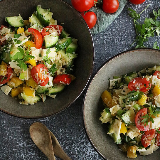 Ein Reissalat-Rezept, serviert in einer grauen Schüssel, mit gelber Paprika, Kirschtomaten, Gurkenstücken und Fol Epi Classic Käse.