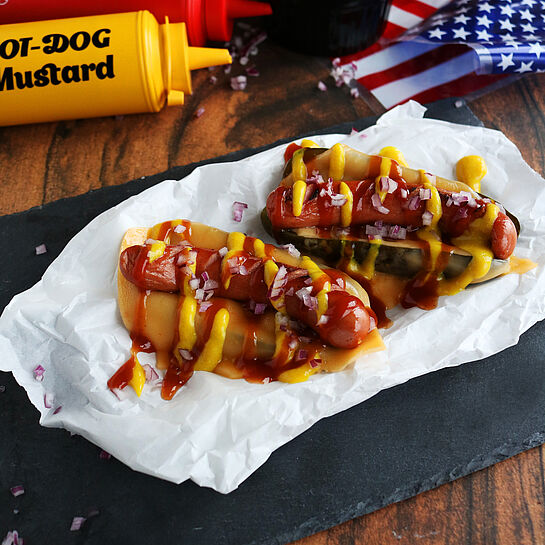 Hot Dog in Gewürzgurke –knackige Gewürzgurke mit Mini-Wiener, garniert mit Zwiebeln, Ketchup und Senf.