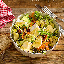 Frühlingsfrischer Salat mit cremigem Camembert und knackigem Gemüse, Haselnusskernen serviert in einer kleinen Schüssel