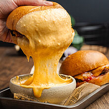 Knuspriger Smashed Burger mit geschmolzenem Cheddar und cremiger Käsesoße, serviert auf goldbraun gerösteten Briochebuns.