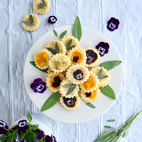 Herzhafte Blütenkekse mit Parmesan und Rosmarin, dekoriert mit essbaren Blüten.
