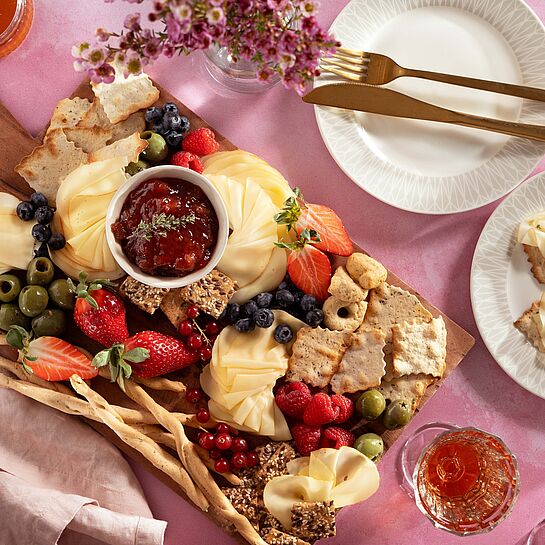 Käseplatte mit Fol Epi Käse, frischen Beeren, Oliven und hausgemachtem Rhabarber-Chutney, angerichtet auf einem rustikalem Holzbrett.