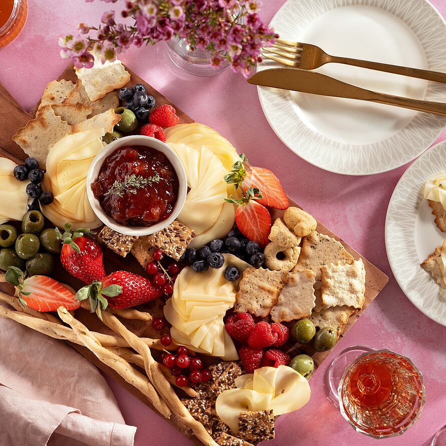 Käseplatte mit Fol Epi Käse, frischen Beeren, Oliven und hausgemachtem Rhabarber-Chutney, angerichtet auf einem rustikalem Holzbrett.