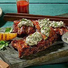 Gegrillte Spareribs mit Orangen-Marinade auf einem Steinbrett mit Saint Agur und Kartoffelhälften garniert. 