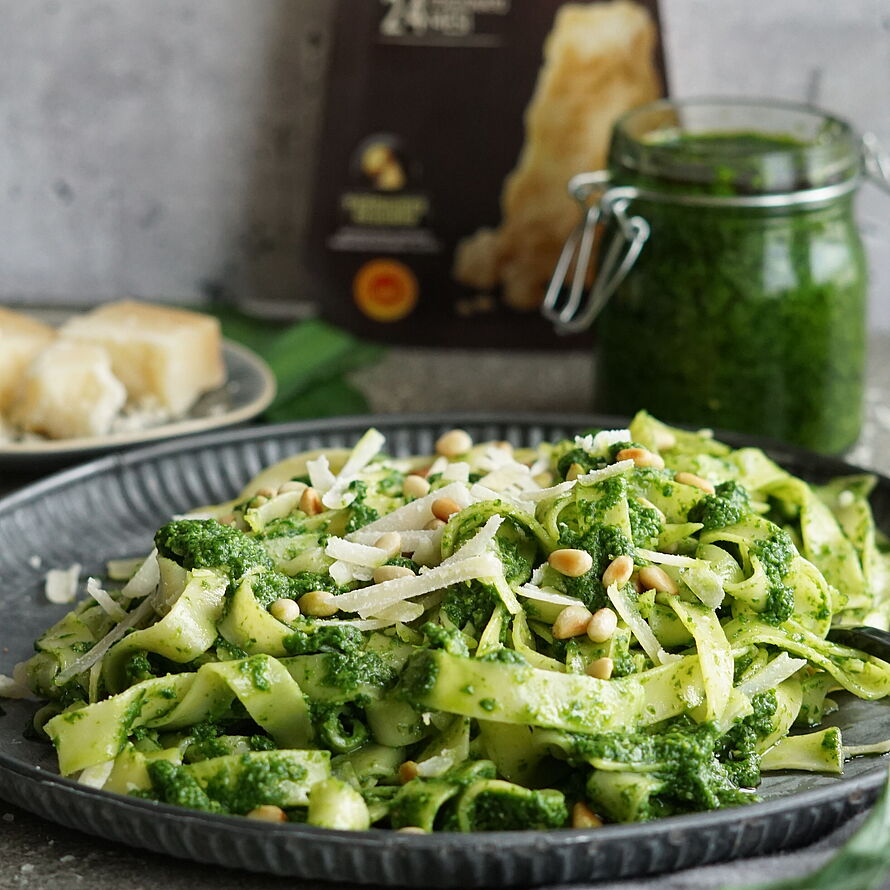 Köstliche Tagliatelle mit Pesto, Parmigiano Reggiano und gerösteten Pinienkernen auf einem Teller angerichtet.