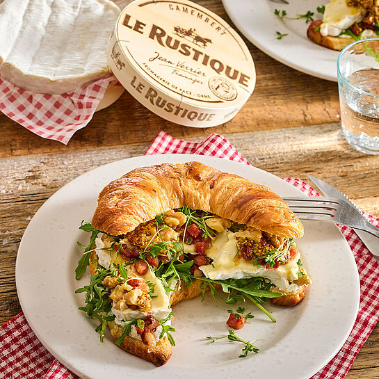 Reichlich belegtes Croissant mit Camembert, Speckwürfel, Walnusskernhälften und Rucola 