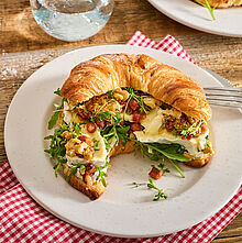 Reichlich belegtes Croissant mit Camembert, Speckwürfel, Walnusskernhälften und Rucola 