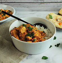 Cremiges Chicken Tikka Masala mit Hähnchenstücken in einer gewürzreichen Tomatensauce, verfeinert mit frischem Koriander.