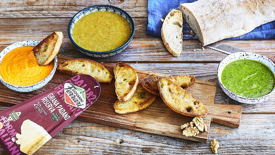 Dreierlei Pestovarianten mit Parmesan, dazu knusprige Crostini auf einem rustialen Holzbrett