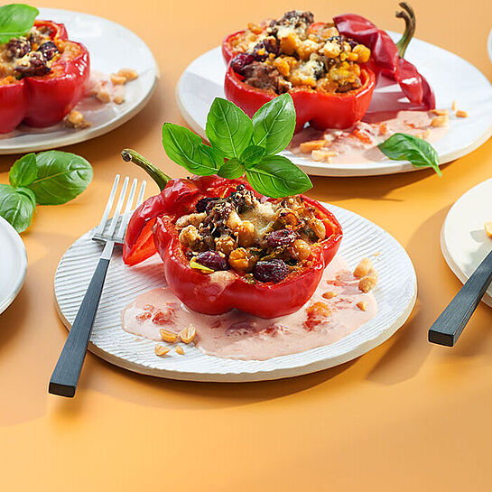 Gefüllte Paprika auf gelbem Grund, angerichtet auf Tellern