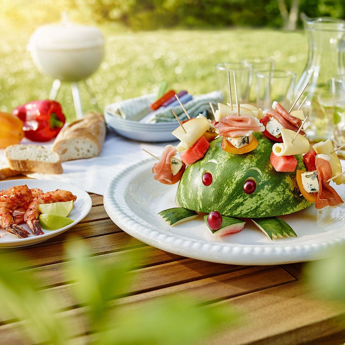 Käseigel Sunny mit Saint Agur, Fol Epi, Parmaschinken und Wassermelone bestückt sitzt auf einem Gartentisch