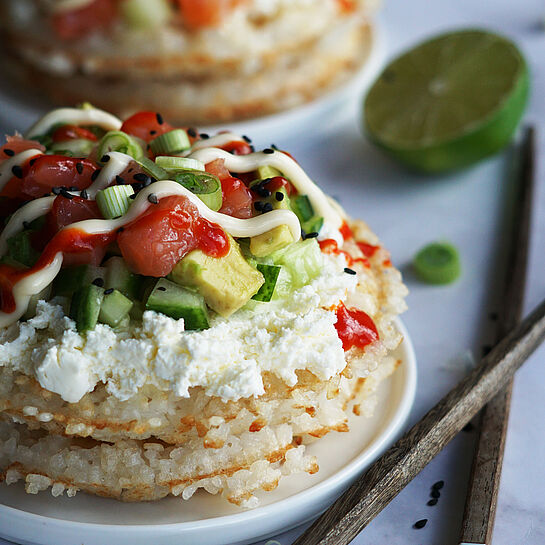 Sushi-Waffeln: Knusprige Waffeln mit Sushireis, frischem Lachs, Avocado, Gurke und Frischkäse, verfeinert mit Sriracha und schwarzem Sesam.