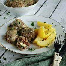 Teller mit Goldrand drauf liegen Königsberger Klopse mit Kapernsoße und Salzkartoffelspalten mit Petersilie. 