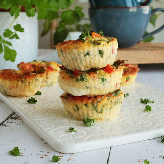 Gestapelte Eiermuffins mit Gemüse und Kräutern auf einer weißen Servierplatte, dekoriert mit frischer Petersilie