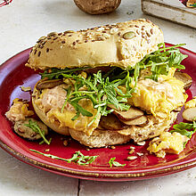 Tolle Frühstückkomposition mit Bagels, Brunch Aufschnitt, Pilzen, Rucola und Rührei. Als Mittelpunkt ein belegtes Frühstückbagel