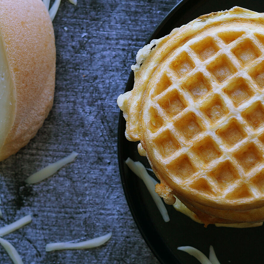 Goldbraun gebackene Keto-Chaffles aus Fol Epi-Käse und Eiern, serviert als Türmchen auf einem Teller. 