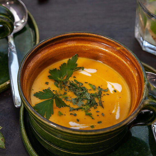 Süßkartoffelsuppe in einer rustikalen Suppenschale serviert und mit frischer Petersilie garniert