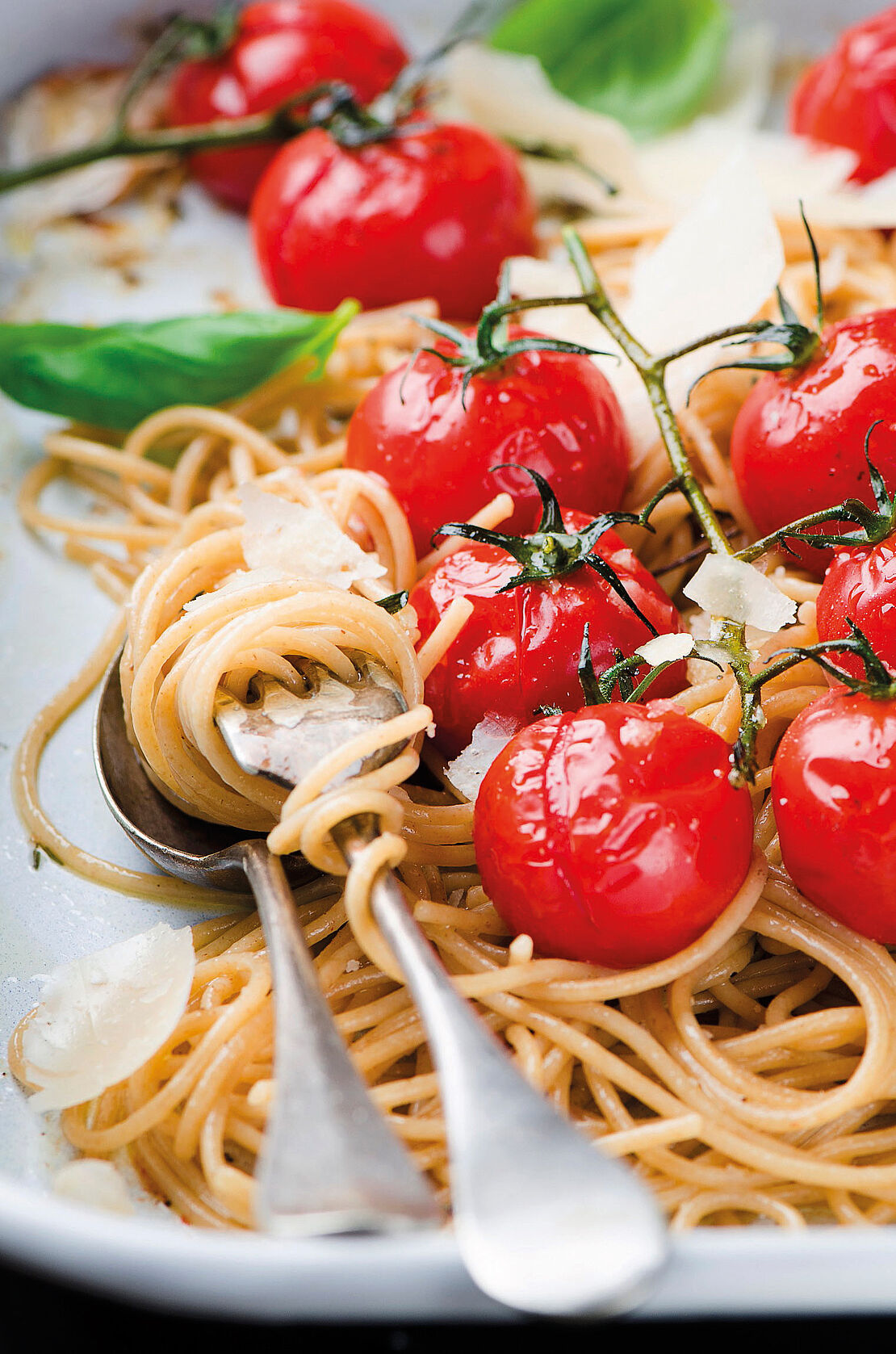 Weißer Teller voller Vollkornspaghetti mit Parmesan, Kirschtomaten und Basilikum