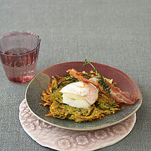 Goldbraun knusprige Rösti aus Zucchini und Kartoffeln garniert auf einem Teller mit Bacon und Saint Albray Käse