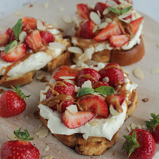 Knuspriges Brioche mit cremiger Frischkäsecreme, marinierten Balsamico-Erdbeeren, Salzkaramell und gehackten Mandeln, garniert mit Basilikum.
