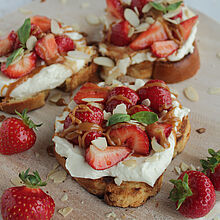 Knuspriges Brioche mit cremiger Frischkäsecreme, marinierten Balsamico-Erdbeeren, Salzkaramell und gehackten Mandeln, garniert mit Basilikum.
